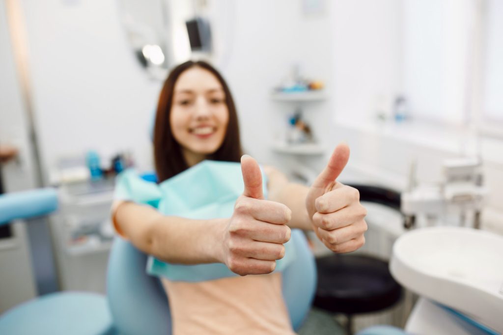 Girl showing thumbs up at a dental clinic reception illustrating what to look for in a dental practice